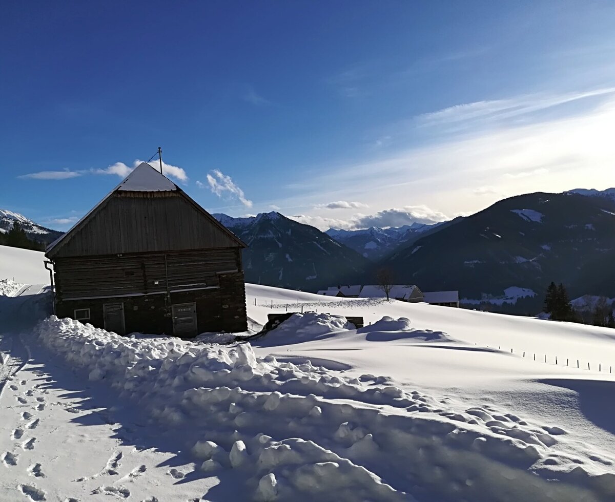 Das traditionelle Holzgebäude des Hofs in einer schneebedeckten Berglandschaft.