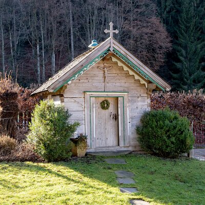Die Hofkapelle aus Holz mit einem Kruzifix über der Tür und einem Kreuz auf dem Dach.
