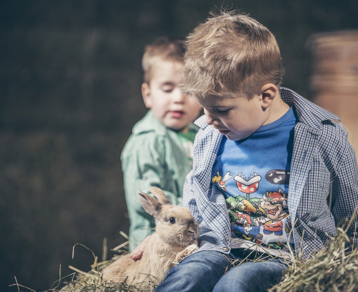 Kinder auf dem Bauernhof streicheln ein Kaninchen auf einem Heuballen.