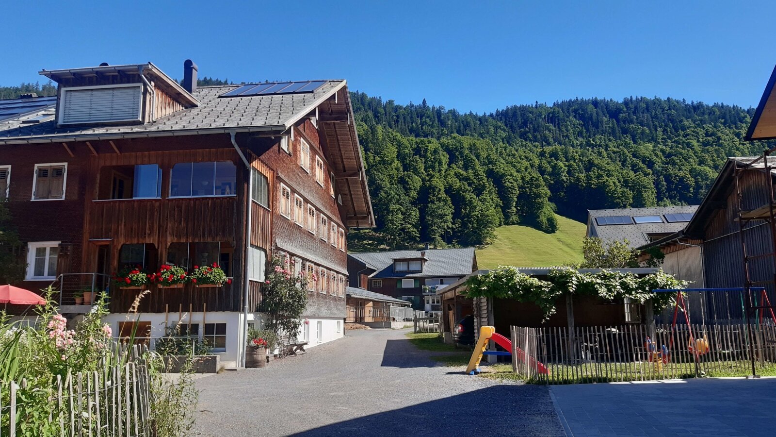 Der Bauernhof mit Holzfassade und Solaranlagen auf dem Dach bietet einen Kinderspielplatz sowie Aussicht auf die umgebenden Berge und Wälder.